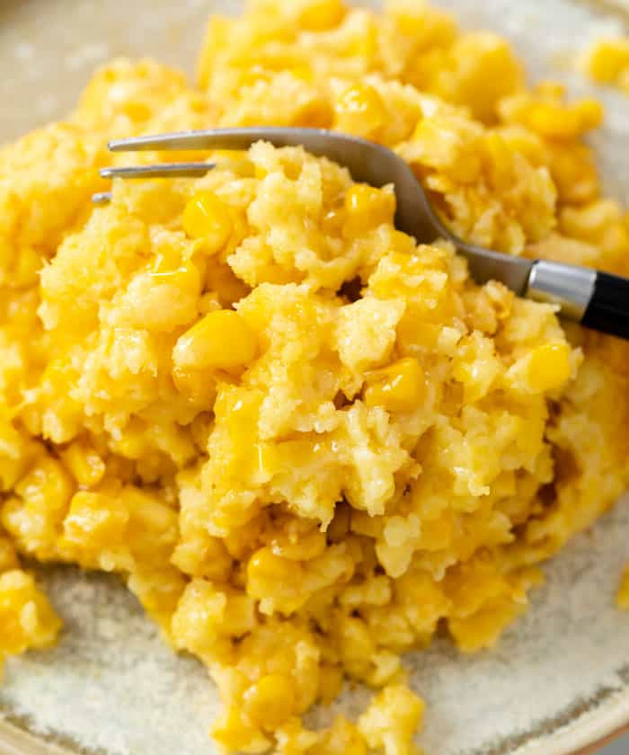 Close-up shot of a spoonful of creamy corn casserole being lifted from a cast iron skillet, showcasing its texture and golden-brown top.