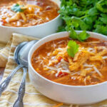 Bowls of Crock Pot Chicken Tortilla Soup garnished with parsley, spoons on the side, suggesting a cozy and inviting meal