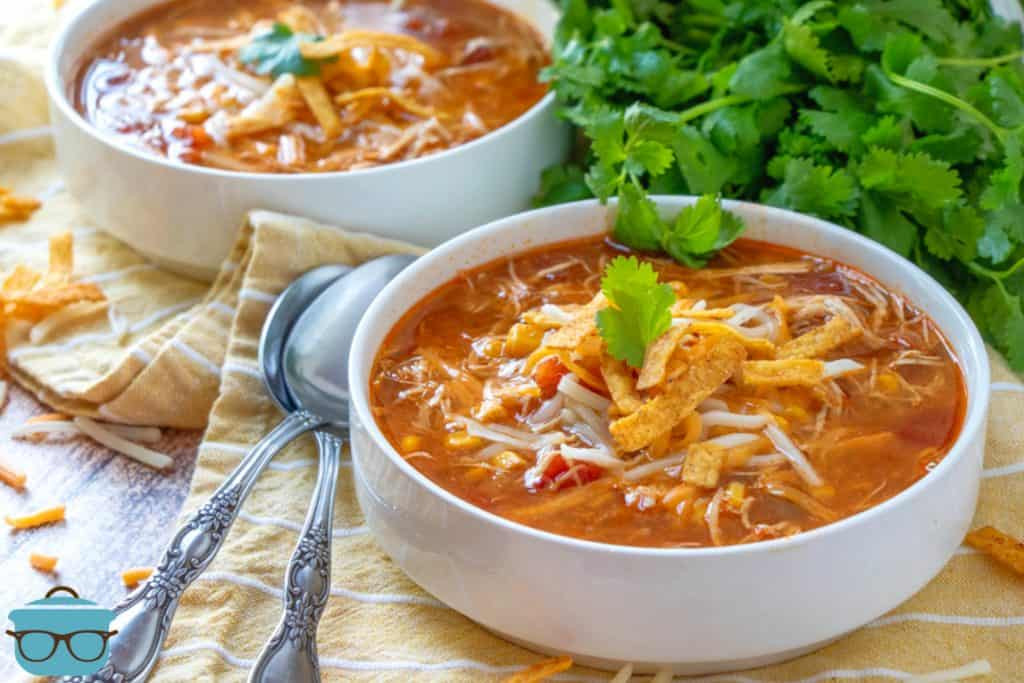 Bowls of Crock Pot Chicken Tortilla Soup garnished with parsley, spoons on the side, suggesting a cozy and inviting meal