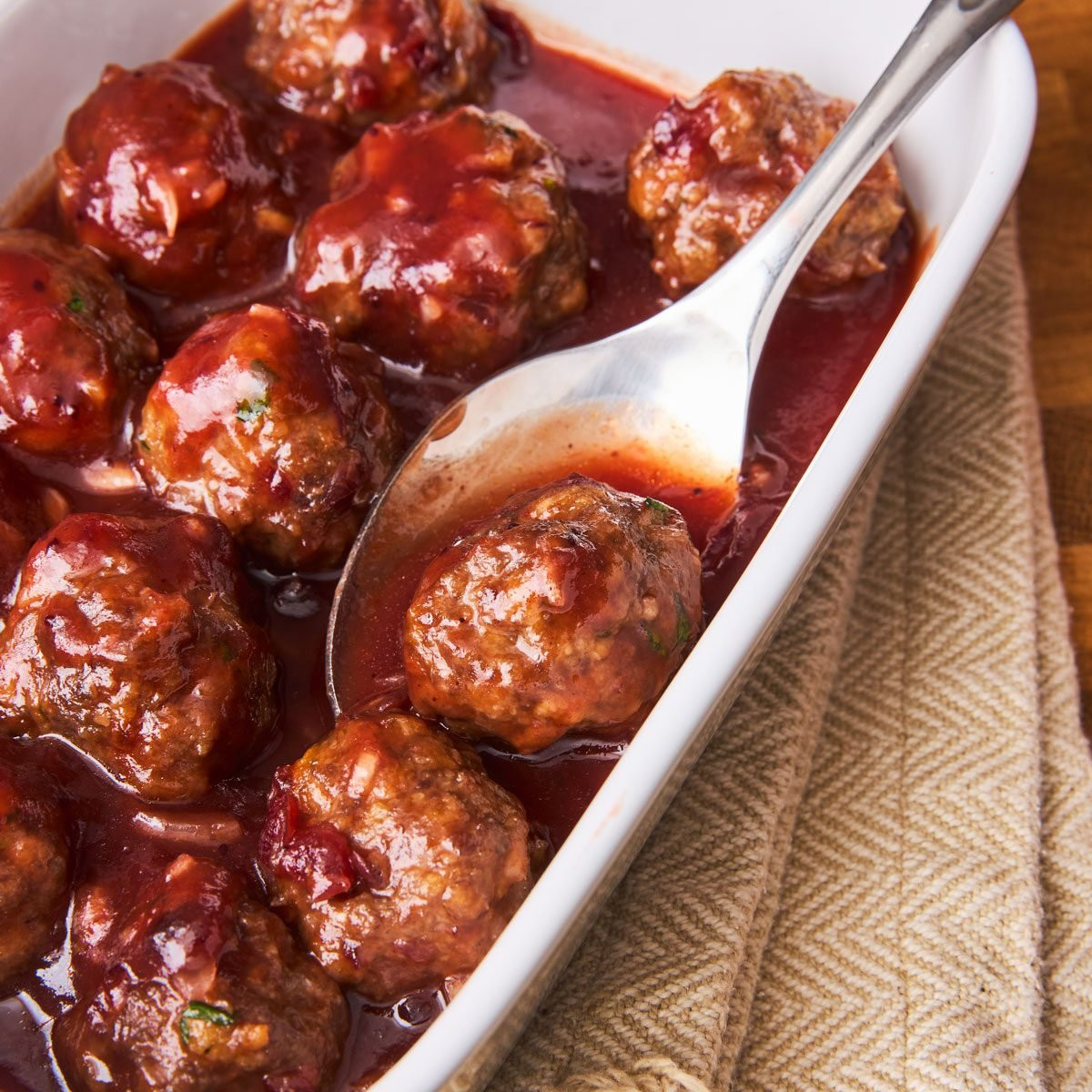 Saucy Meatballs, meatballs in a cranberry sauce, served in a white dish.