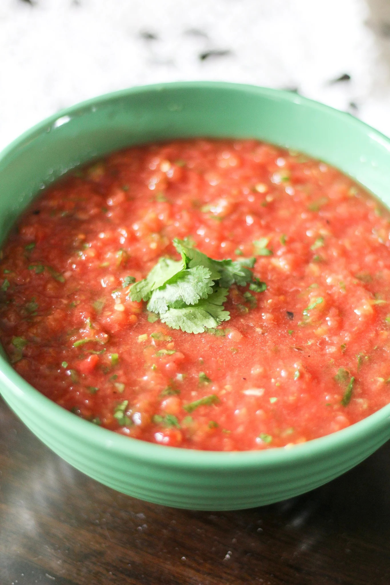 Jar of homemade Pioneer Woman Restaurant Salsa with visible chunks of tomatoes, onions, and cilantro, sitting on a kitchen counter next to a knife and cutting board with lime.