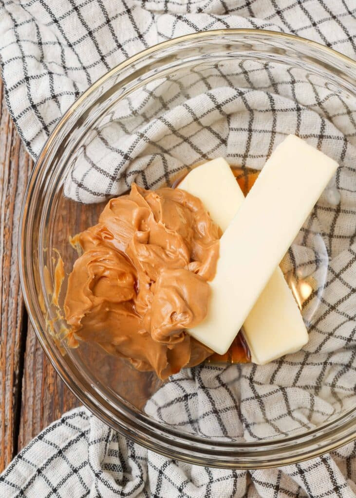 Close-up of fudge ingredients in a clear glass bowl, highlighting butter, peanut butter, and powdered sugar.