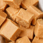 Creamy peanut butter fudge squares on parchment paper, showcasing its smooth texture and inviting color.