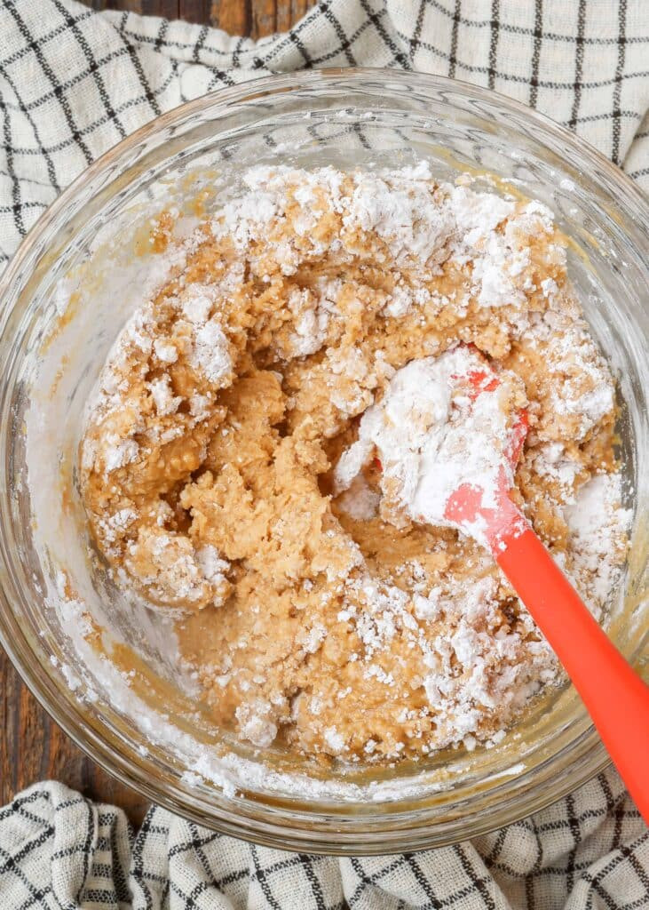 Fudge mixture being stirred in a bowl, showing its thick and almost crumbly texture before being pressed into a pan.