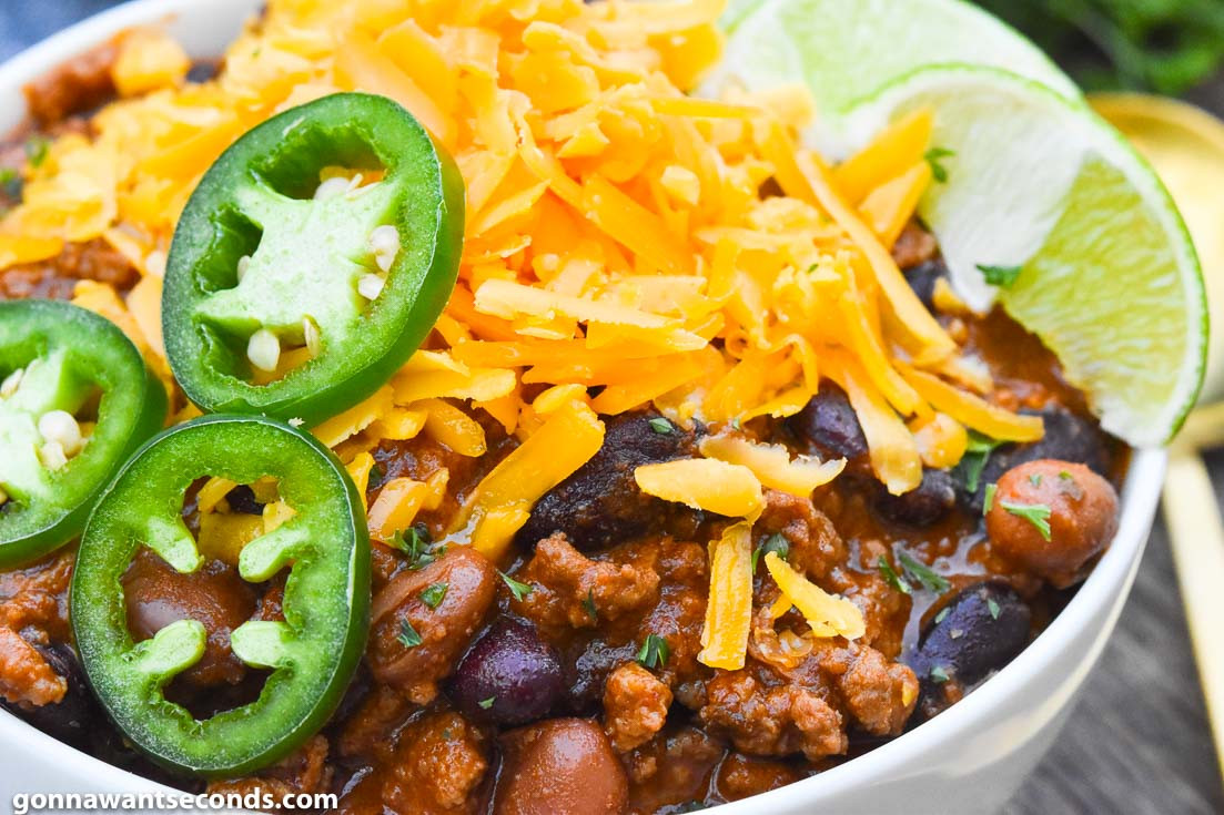 Bowl of Pioneer Woman chili topped with cheese, jalapeno, and lime wedges