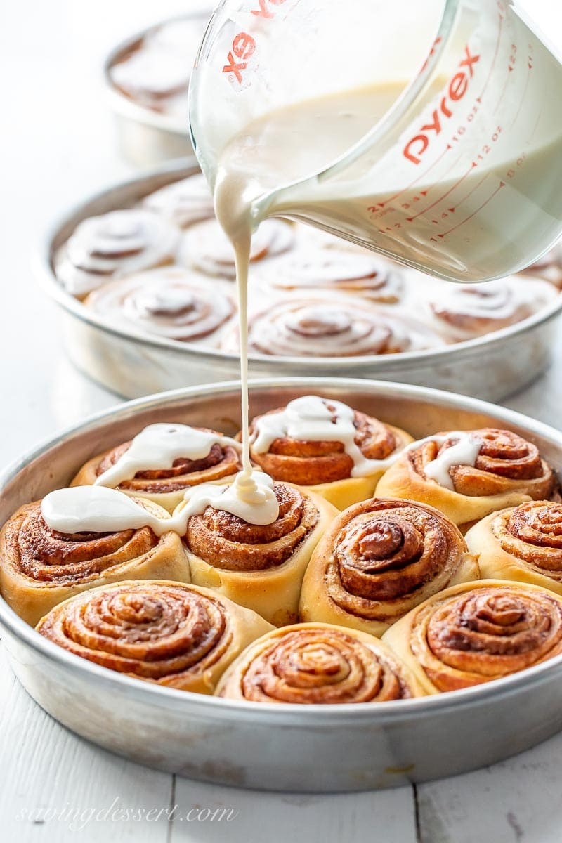 A pan of cinnamon rolls being drizzled with a maple frosting