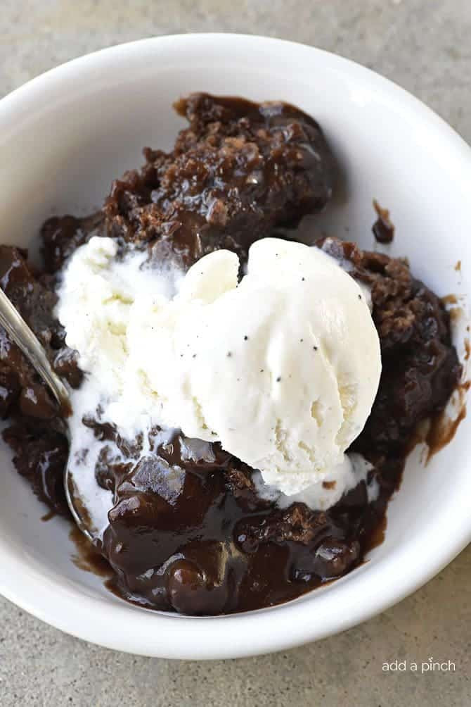 Close-up of chocolate cobbler in a white bowl, topped with a scoop of vanilla ice cream and a spoon resting in the bowl.