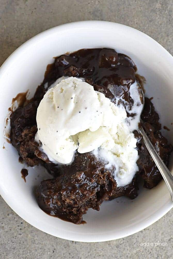 A single serving of chocolate cobbler in a white bowl with a spoon, topped with a scoop of melting vanilla ice cream.