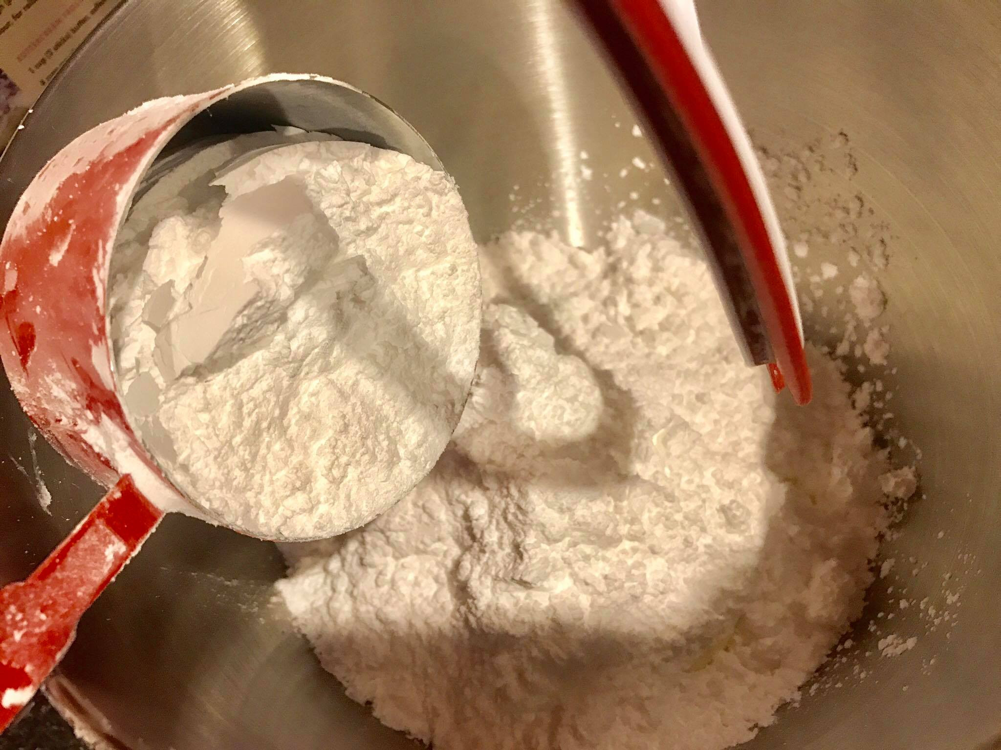 Adding powdered sugar to softened butter in a mixing bowl