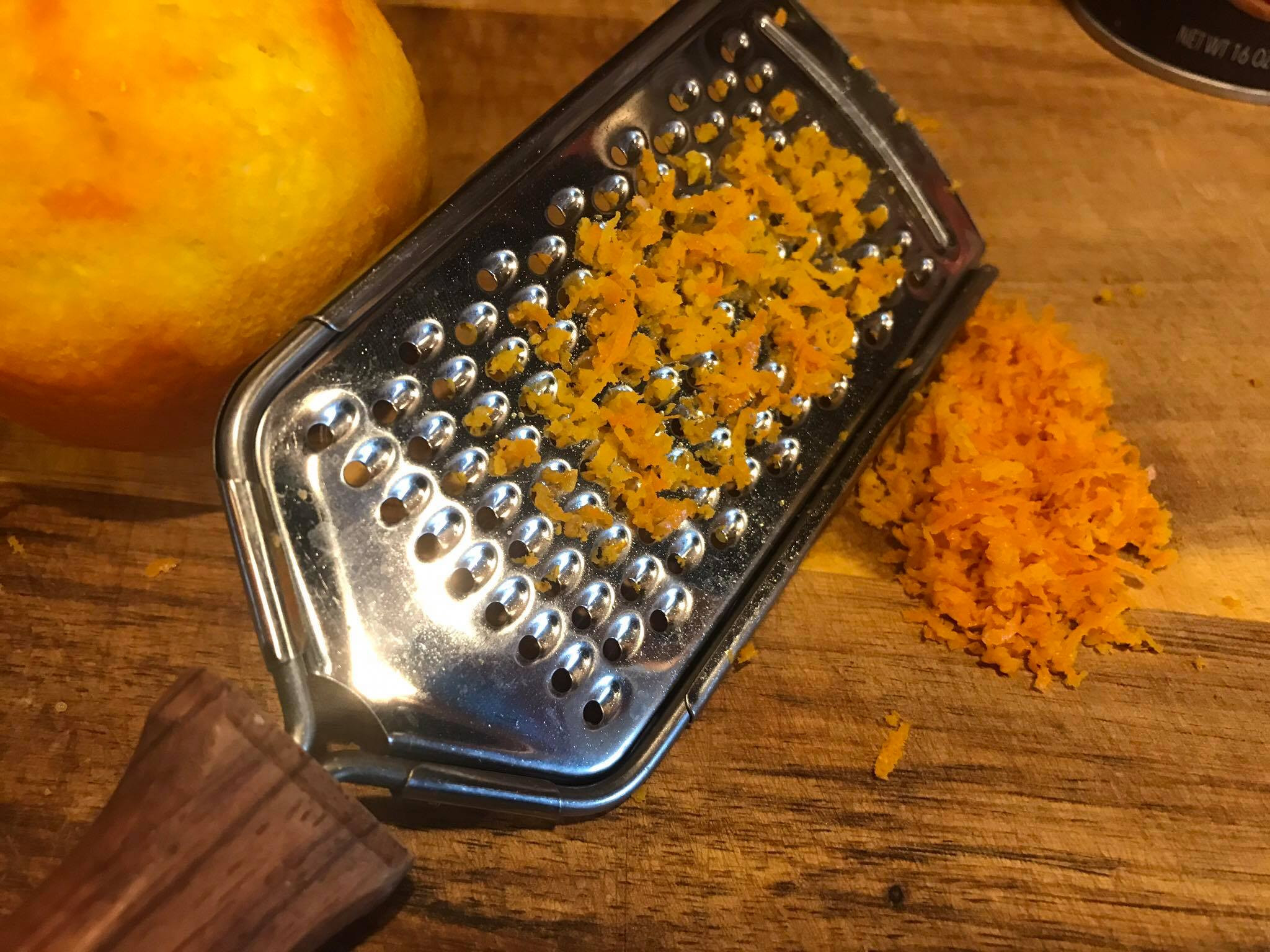 Hands grating fresh orange zest into a small white bowl