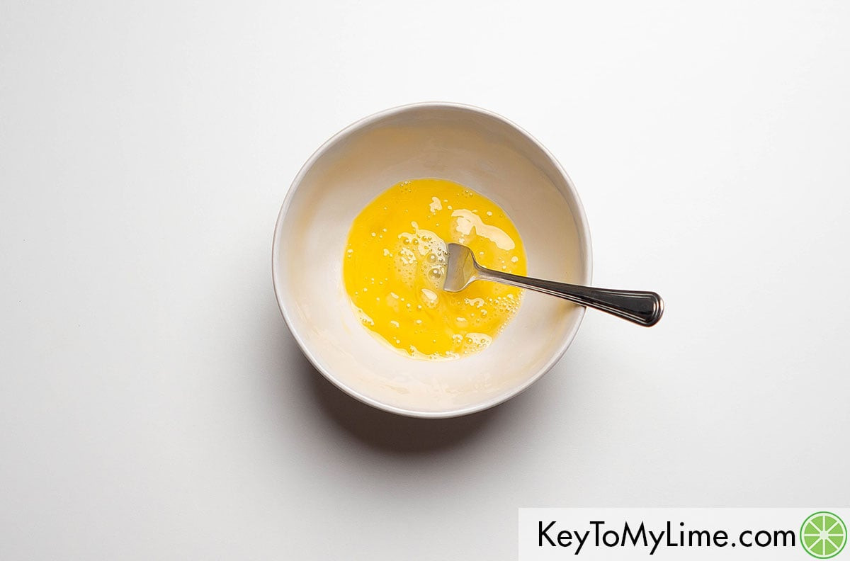 Beating an egg in a small mixing bowl with a fork.