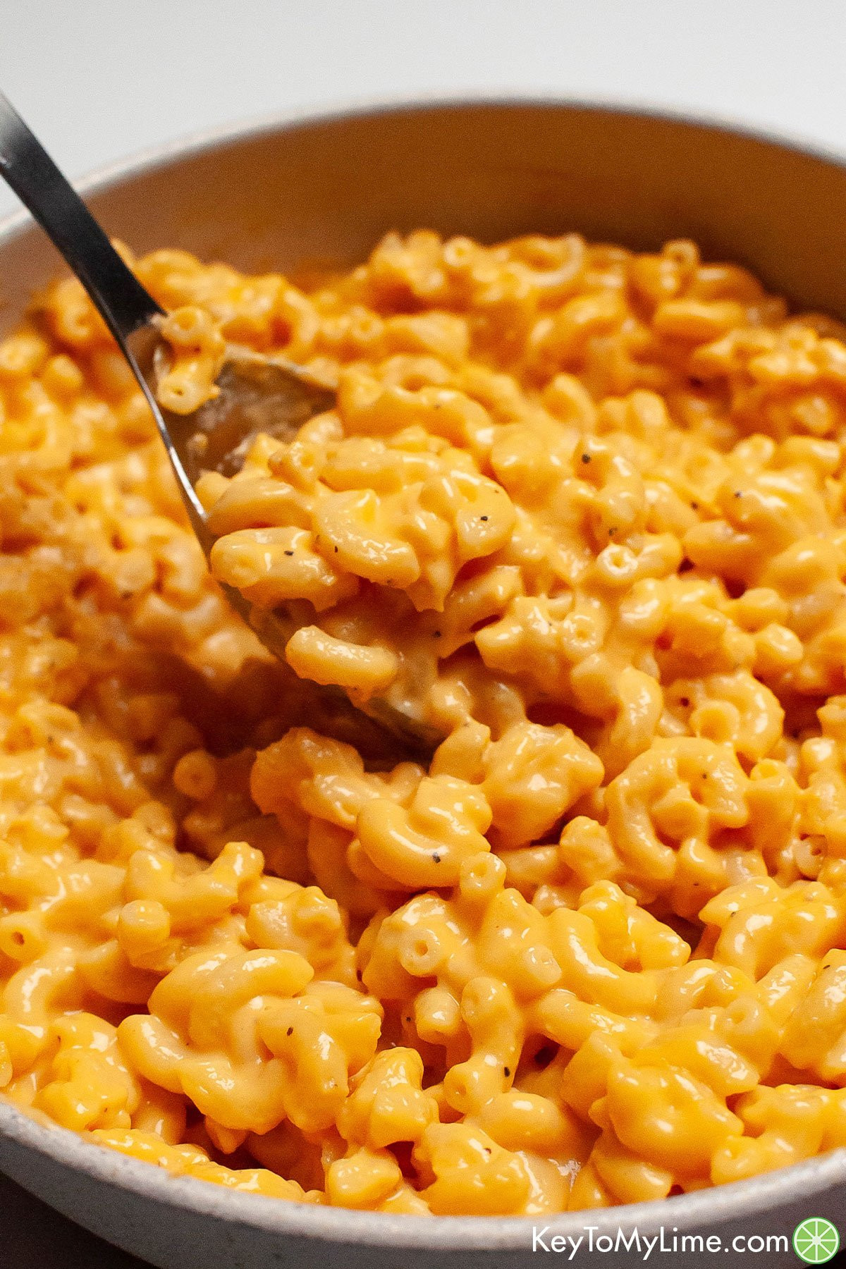 A serving spoon with a scoop of mac and cheese in a large pot.