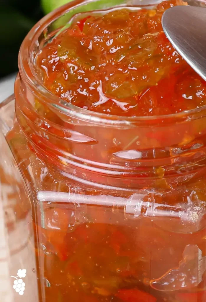 A person carefully pouring hot jalapeno jelly from a large pot into sterilized glass jars, using a ladle for precise pouring.