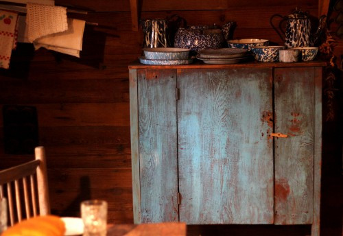 A vintage blue cupboard filled with antique items inside a Hart Square cabin, showcasing pioneer-era furniture