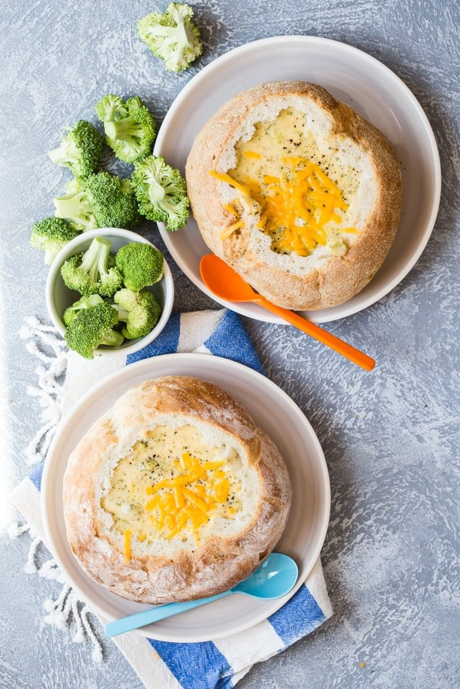 Overhead shot of broccoli cheddar soup in a white bowl with bread and a spoon