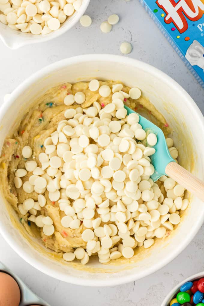 Mixing funfetti cake mix batter for cookie bars with white chocolate chips.