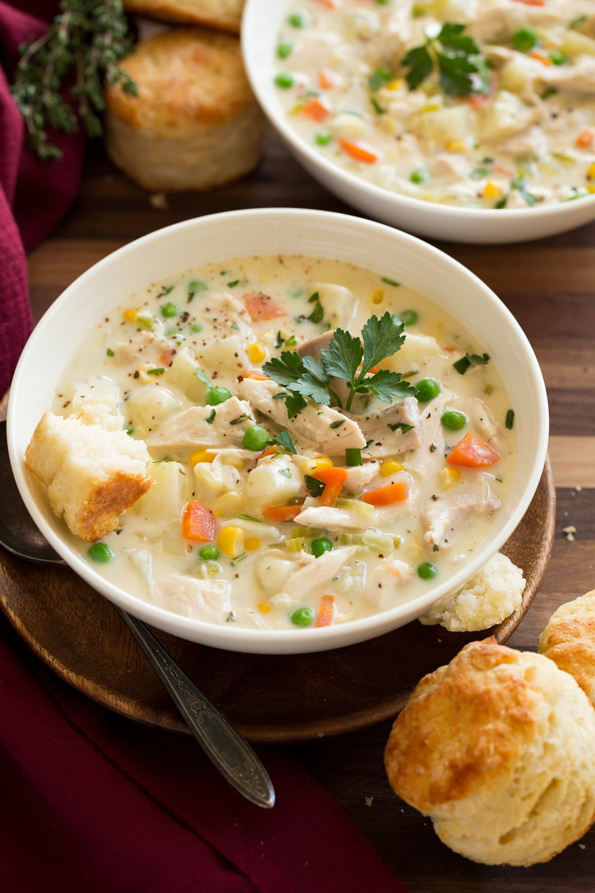 Bowls of creamy chicken pot pie soup garnished with fresh herbs and served with flaky biscuits on a rustic wooden table.