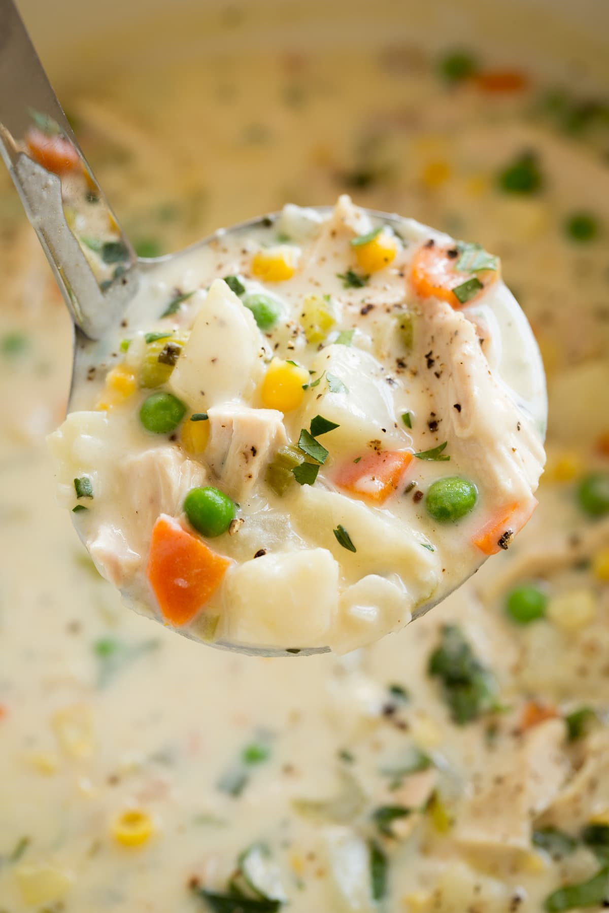 A close-up shot of a ladle scooping up a spoonful of creamy chicken pot pie soup, showcasing the chunks of chicken and vegetables.