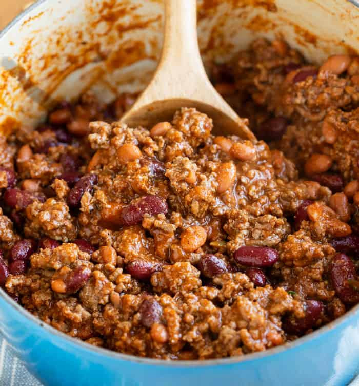 Close-up of chili being scooped with a wooden spoon from a pot, showcasing its rich texture.