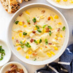 bowl of corn chowder with bacon pieces green onions and bread on the side.