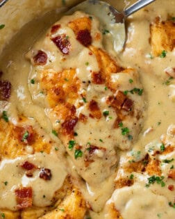 Image of Smothered Chicken coated in gravy and garnished with crispy bacon and parsley.