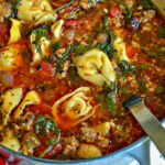 A hearty dutch oven filled with sausage and cheese tortellini soup, ready to be served.