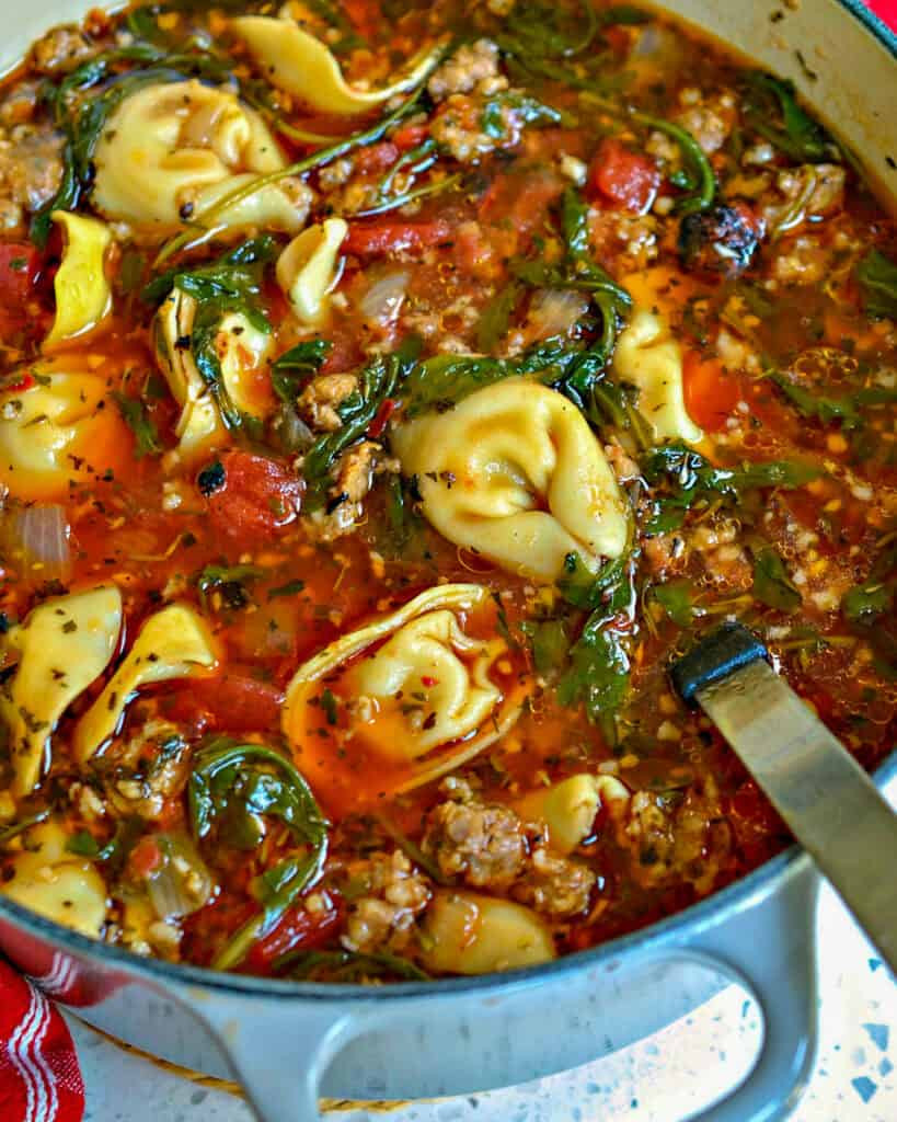 A hearty dutch oven filled with sausage and cheese tortellini soup, ready to be served.