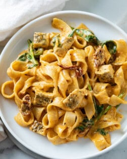 Image of creamy Tuscan Chicken Pasta with spinach and chicken on a white plate.
