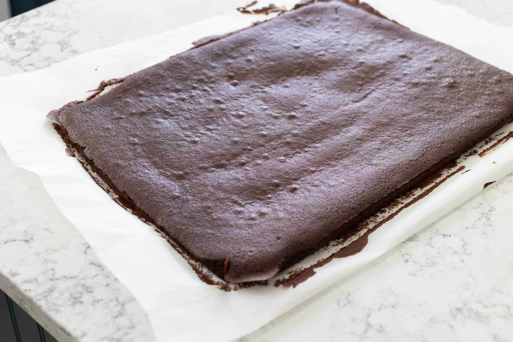 Freshly baked chocolate sponge cake for Yule Log, cooling on parchment paper on a kitchen counter.