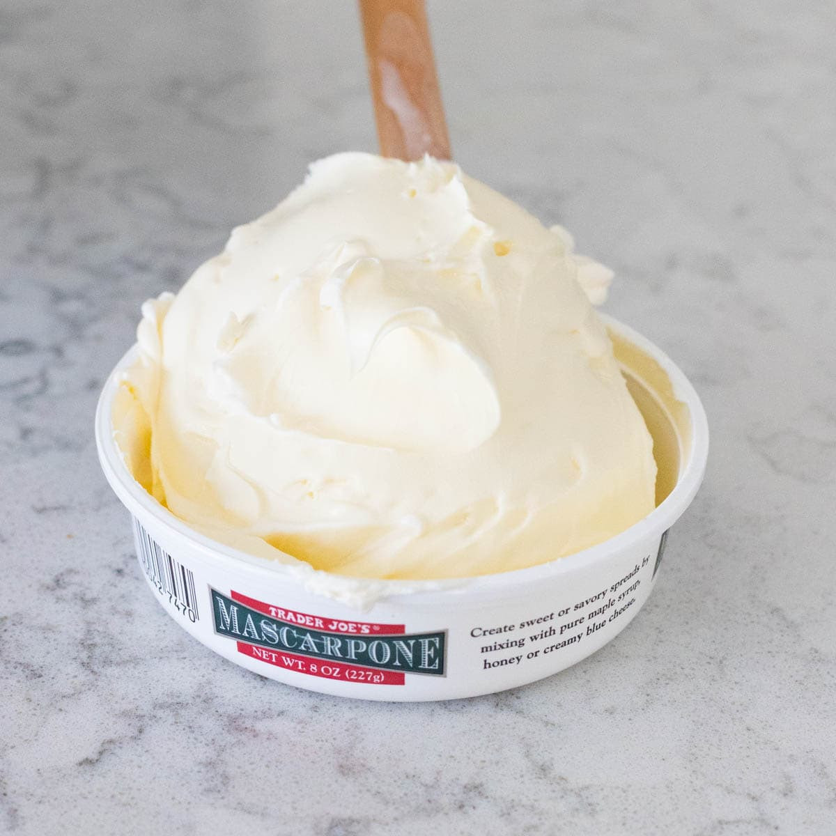 Softened mascarpone cheese in its container on a kitchen counter, ready to be used for the Yule Log cake filling.