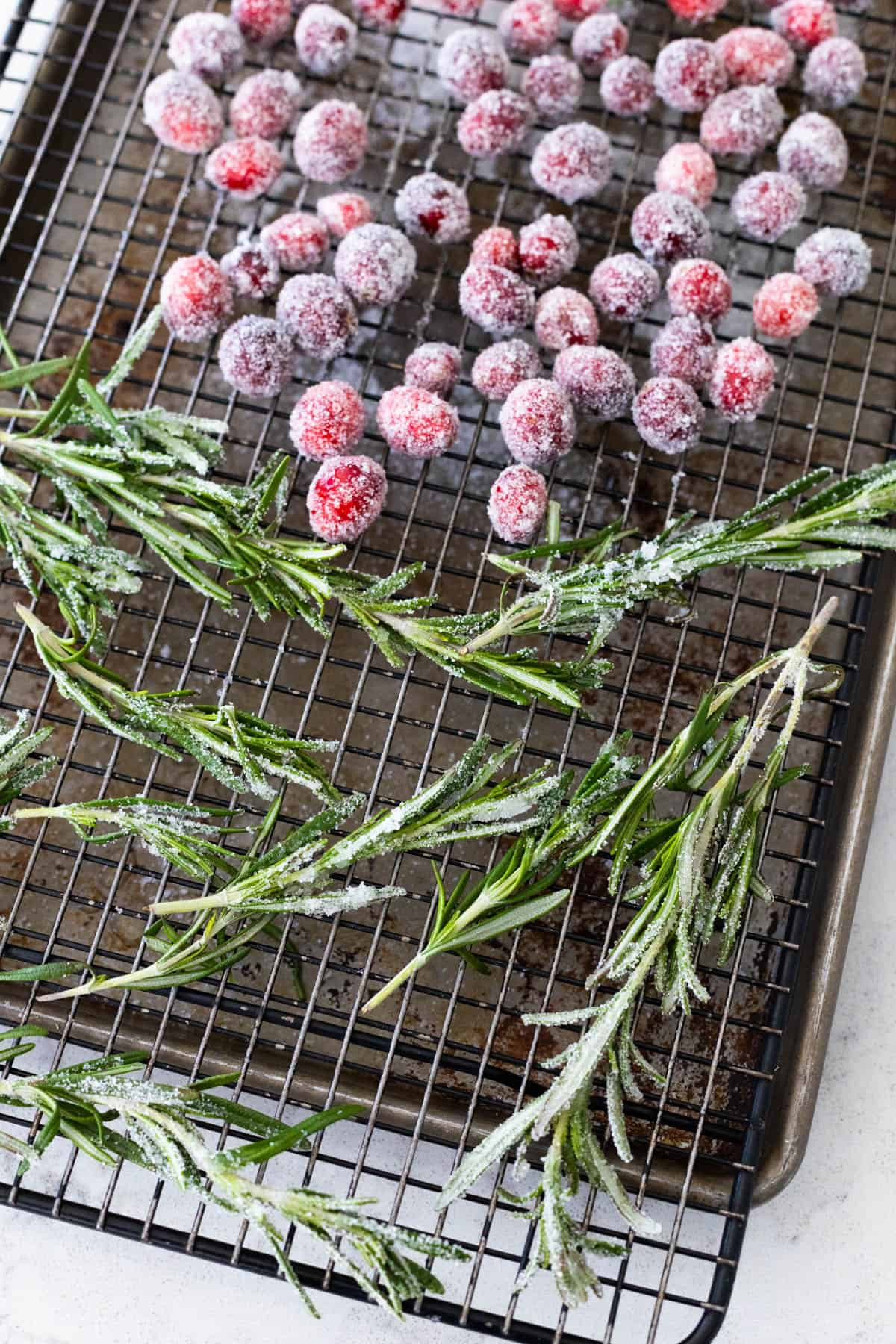 Sugared rosemary sprigs and cranberries drying on a wire rack, ready to be used as decorations for the Pioneer Woman Yule Log cake.